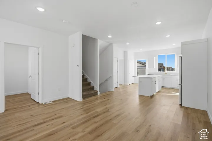 Open-concept interior featuring light wood-finish flooring, recessed lighting, a kitchen island with white cabinetry, and carpeted staircase