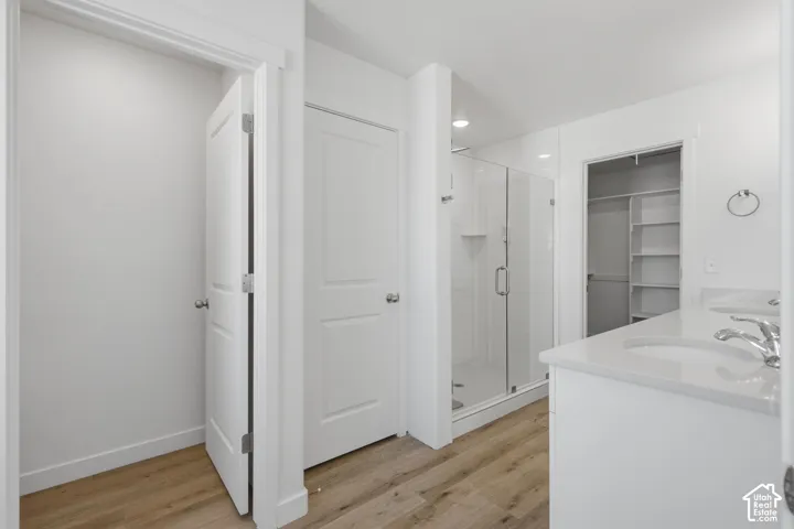 Double vanity with quartz countertops, wood-finish flooring, glass-enclosed shower with tile surround, and integrated walk-in closet shelving