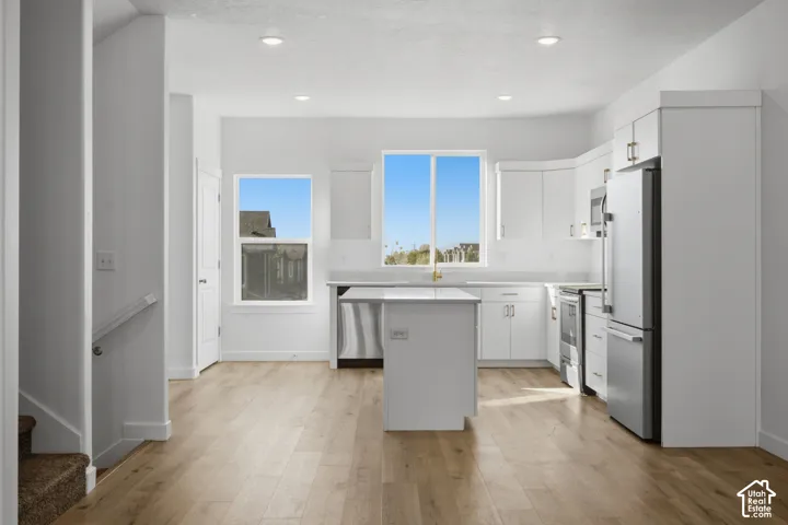 Kitchen featuring white cabinetry, an island with stone-finish countertops, stainless steel appliances, and wood-finish flooring