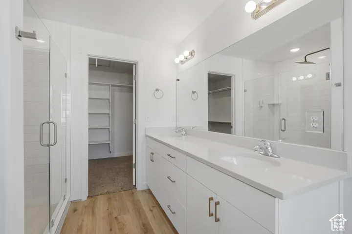 Double vanity with solid surface countertops, frameless glass-enclosed shower with subway tile surround, expansive wall-mounted vanity mirror, and wood-finish flooring