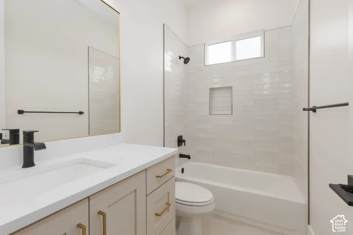 Bathroom featuring a vanity with white stone countertop, matte black faucet, wall-mounted mirror with gold frame, and a tub with horizontal subway tile surround and built-in niche