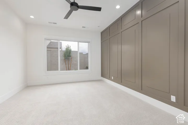 Room featuring a decorative paneled accent wall, neutral carpeting, recessed ceiling lighting, and a matte black finish ceiling fan