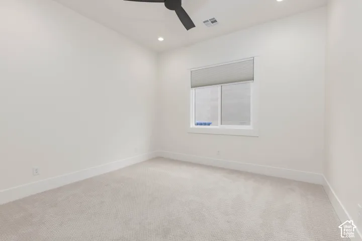 Neutral-toned wall-to-wall carpeting, recessed ceiling lighting, matte black ceiling fan, and a window with a fitted pleated shade