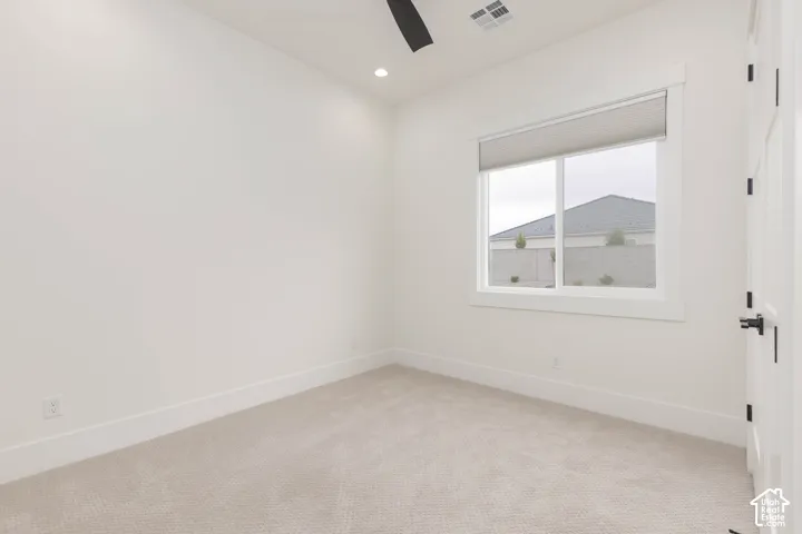 Neutral-toned wall-to-wall carpeting, crisp white walls, recessed ceiling lighting, a matte black ceiling fan, and a single-hung window with a cellular shade