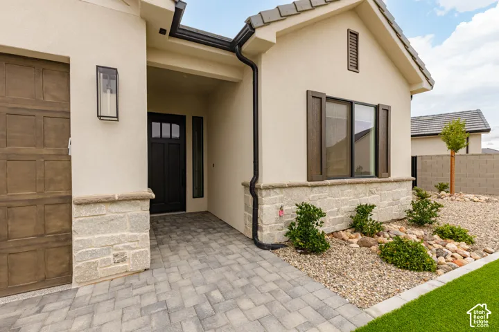 Stucco exterior with stone masonry veneer, paved walkway, dark-tone shutters, recessed front entryway, and metal-frame light fixture
