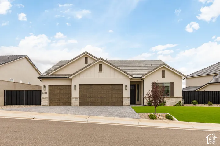 Single-story exterior featuring light stucco siding, stone veneer accents, a multi-gabled roofline, a paver driveway, and a three-car garage