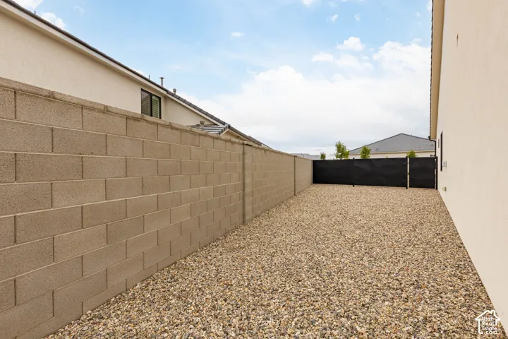 Side yard featuring decorative stone ground cover, a concrete block wall perimeter, and a metal privacy gate