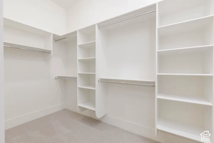 Walk-in storage space featuring built-in white shelving units, multiple tiered hanging rods, and neutral carpeting
