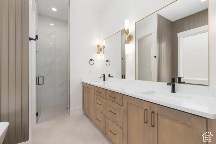 Double vanity featuring light wood-finish cabinetry, white stone-composite countertops, matte black plumbing fixtures, oversized mirrors with gold-tone frames, and vertical accent wall paneling