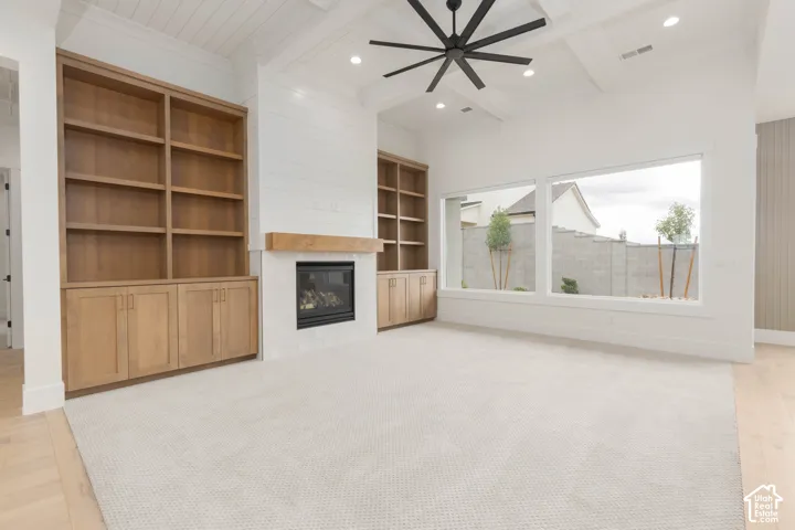 Living area featuring a coffered ceiling with a multi-blade fan, dual built-in shelving units, a central fireplace with a wood mantel, and expansive horizontal windows