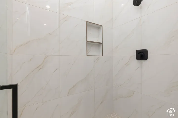 Walk-in shower featuring large-format white tile with gold veining, a built-in recessed wall niche, matte black shower fixtures, and a glass door