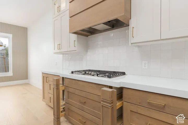Kitchen featuring two-tone custom cabinetry, stone-surface countertops, square-tiled backsplash, integrated gas cooktop, and wood-finish flooring