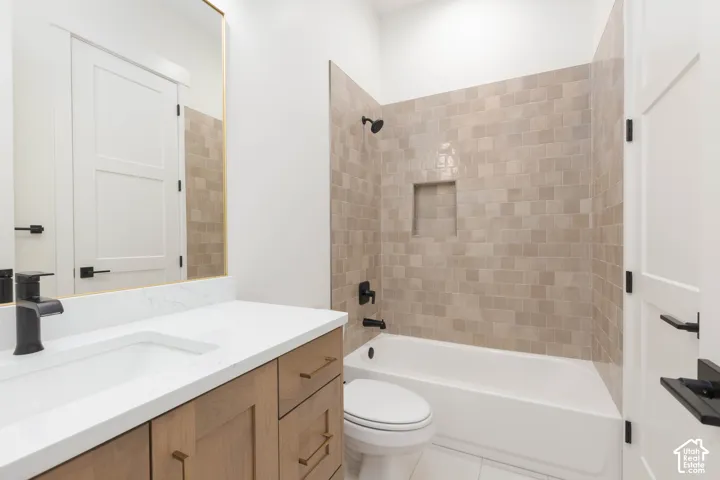Bathroom featuring a vanity with a white countertop and rectangular undermount sink, matte black hardware, wood-finish cabinetry, a tub-shower combination with square wall tile, and a built-in shower niche