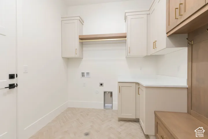 Utility room featuring herringbone-patterned tile flooring, custom cabinetry with brushed gold hardware, a stone-surface countertop, and built-in wood-finish shelving with an integrated hanging rod