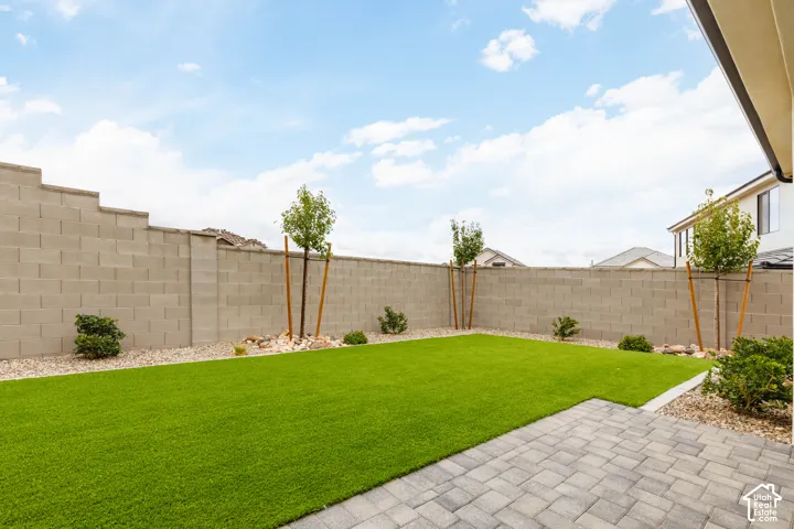 Rear yard featuring a paved stone patio, artificial turf lawn, decorative gravel borders, and concrete block perimeter wall