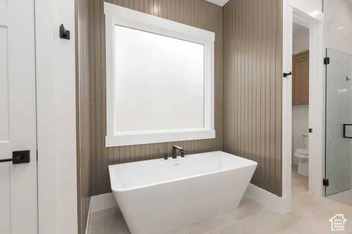 Freestanding white soaking tub with matte black fixtures, vertical tongue-and-groove wall paneling, and ceramic tile flooring