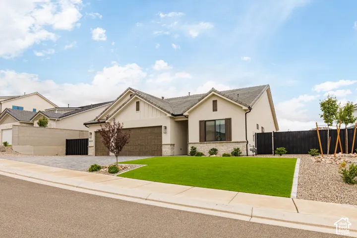 Single-story stucco exterior featuring a concrete tile roof, stone masonry accents, a two-car garage, and manicured landscaping