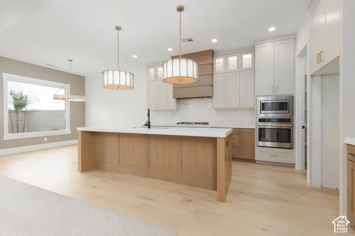 Kitchen featuring wood-finish flooring, a central island with a solid-surface countertop, custom cabinetry, a built-in double oven, and designer drum pendant lighting