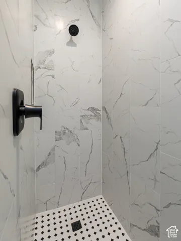 Shower featuring large-format marble-look wall tiles, black and white mosaic floor tiles, a matte black shower head, and a matte black shower control