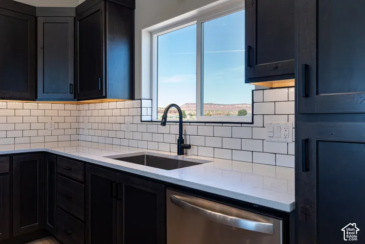 Kitchen featuring dark wood cabinetry, white subway tile backsplash, white countertops, and a stainless steel dishwasher