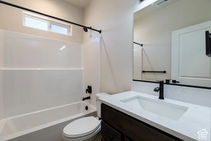 Integrated bathtub with a shower, dark wood-finish vanity with an integrated sink, polished countertop, and matte black fixtures