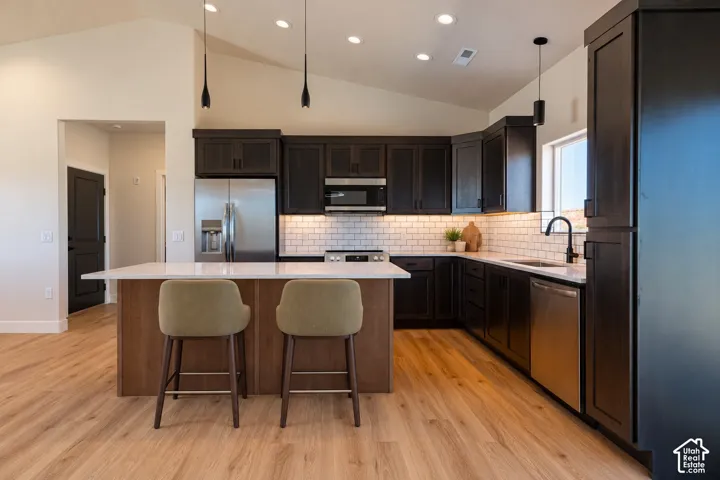 Kitchen featuring dark wood cabinetry, a central island with quartz countertops, subway tile backsplash, stainless steel appliances, and wood-finish flooring