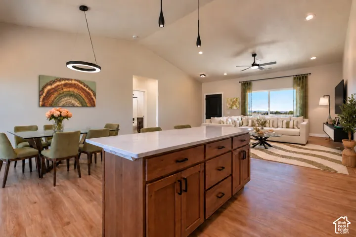 Kitchen island with stone countertop and wood-finish cabinetry, vaulted ceilings, pendant lighting, recessed lighting, and wood-finish flooring