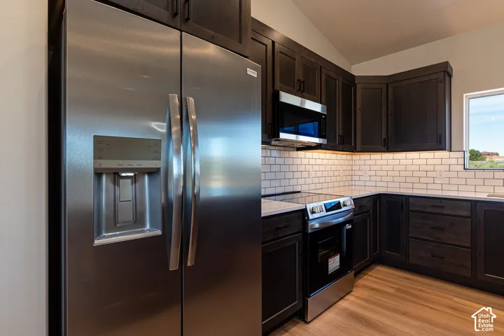 Kitchen featuring dark-stained cabinetry, stainless steel appliances, subway tile backsplash, light-toned countertops, and wood-finish flooring
