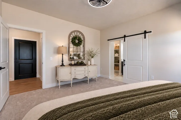 Interior space featuring neutral carpeting, a white barn door with matte black hardware, a black paneled entry door, and a modern ceiling fan