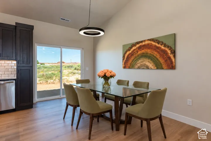 Vaulted ceiling featuring a contemporary circular ring pendant light, wood-finish flooring, dark cabinetry, and sliding glass doors