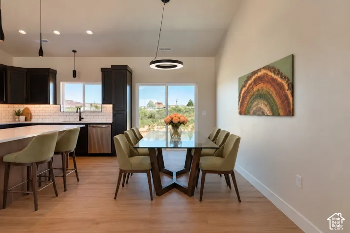 Kitchen featuring dark cabinetry, subway tile backsplash, stainless steel appliances, wood-finish flooring, and a modern circular pendant light