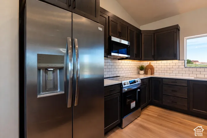 Kitchen featuring dark-finish cabinetry, stainless steel appliances, subway tile backsplash, quartz countertops, and wood-finish flooring