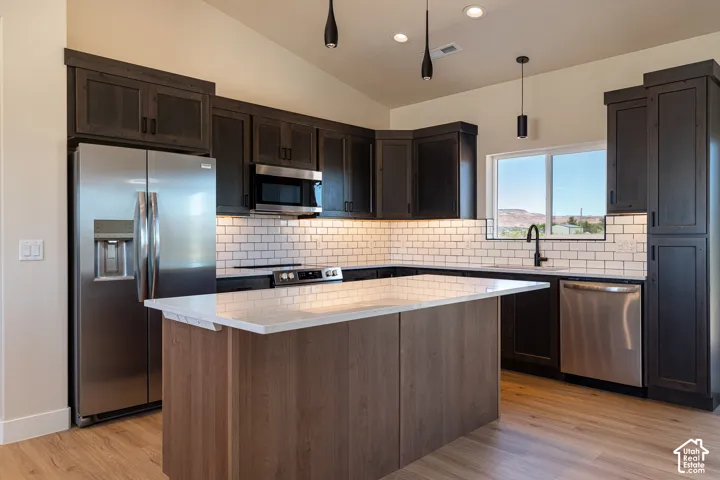 Kitchen featuring dark wood cabinetry, stainless steel appliances, light wood-finish flooring, a kitchen island with light countertop, and a white subway tile backsplash