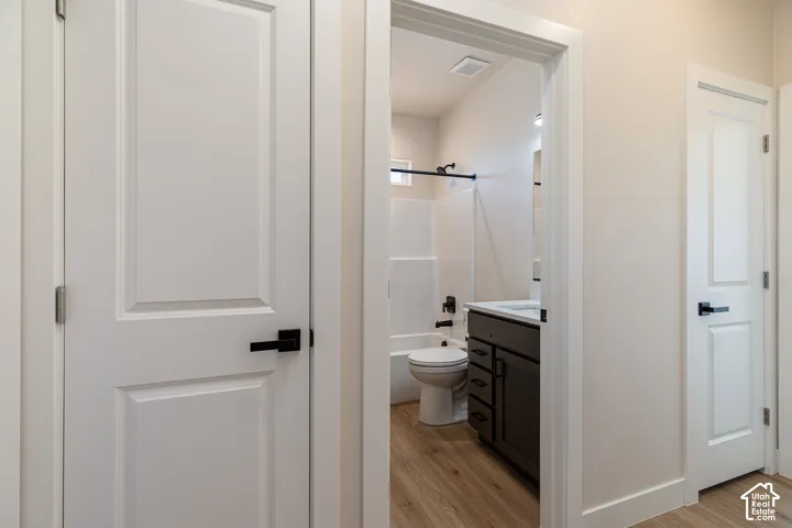 Bathroom featuring a dark wood-finish vanity with an integrated sink, white tub with shower, and wood-finish flooring