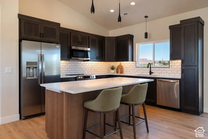 Kitchen featuring dark cabinetry, white quartz countertops, subway tile backsplash, stainless steel appliances, and wood-finish flooring