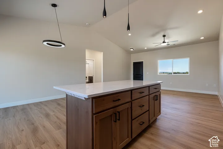 Kitchen island with white countertop and wood-finish cabinetry, vaulted ceiling, wood-finish flooring, recessed lighting, and a window providing natural illumination