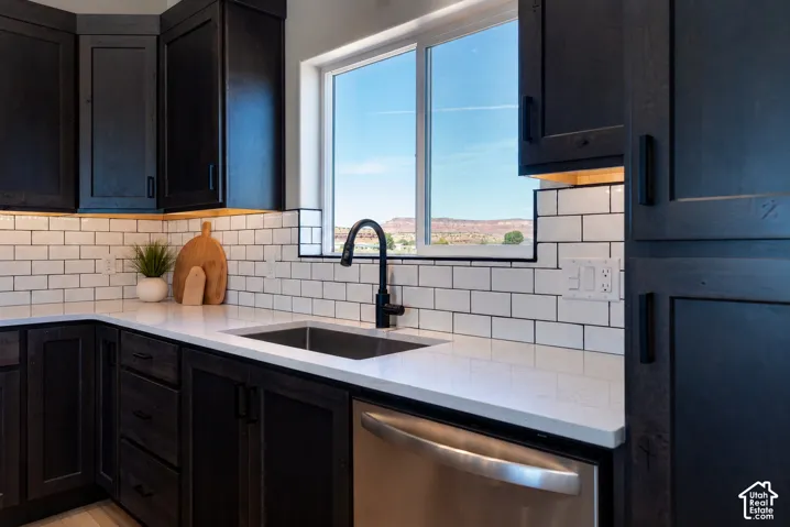 Dark-stained cabinetry, light-toned stone countertops, white subway tile backsplash, stainless steel dishwasher, and high-arc matte black faucet