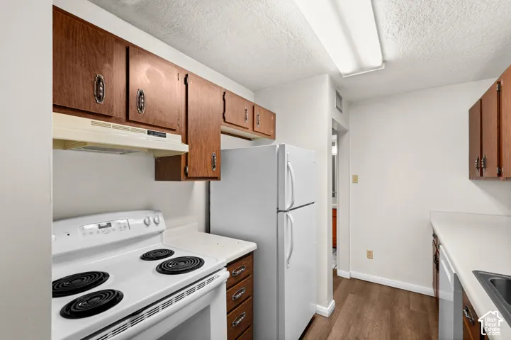 Kitchen featuring wood cabinetry, white appliances, solid surface countertops, and wood-finish flooring