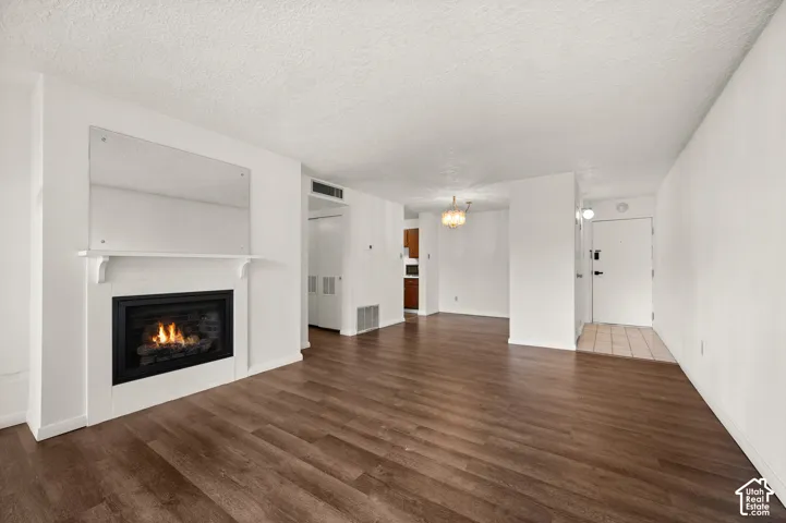 Living area featuring wood-finish flooring, white fireplace mantel with a built-in mirror, stone-tiled entryway, and a tiered chandelier