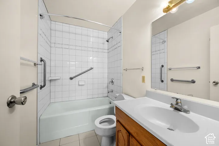 Bathroom featuring a wood-finish vanity with a white integrated sink, a shower-tub combination with white tile surround, and a wall-mounted vanity mirror