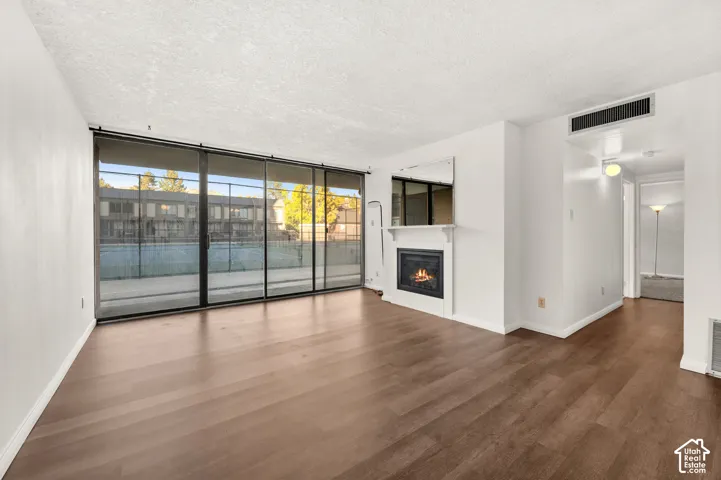 Open-concept living space featuring wood-finish flooring, floor-to-ceiling glass sliding doors, and a fireplace with a white mantel and over-mantel mirror
