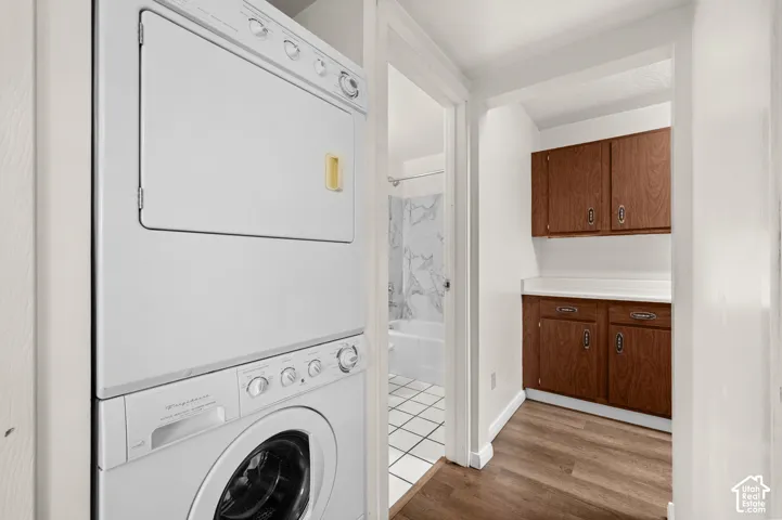 Utility area featuring a stacked laundry unit, wood-finish cabinetry, countertop workspace, and wood-finish flooring