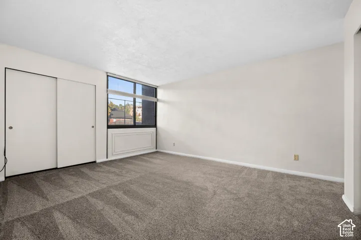Neutral-toned wall-to-wall carpeting, large window with natural lighting, sliding-door closet, and built-in wall-mounted heating unit