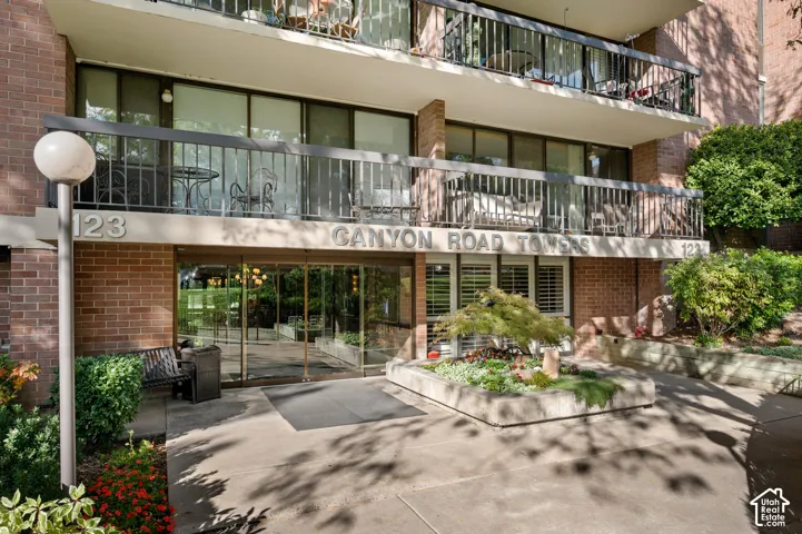 Brick exterior building featuring multi-level balconies with metal railings, a glass-enclosed entrance, and a concrete masonry landscape planter