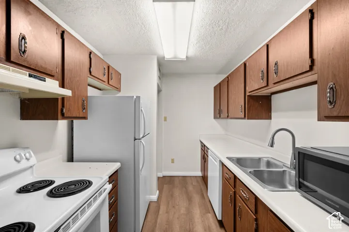 Kitchen featuring wood-finish cabinetry, white solid-surface countertops, wood-finish flooring, dual-basin stainless steel sink, and flush-mount linear lighting