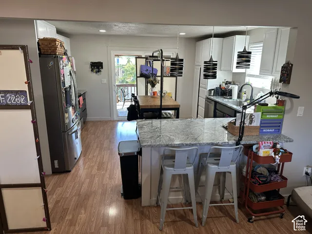 Kitchen featuring stone countertops, white cabinetry, wood-finish flooring, stainless steel appliances, and tiered pendant lighting