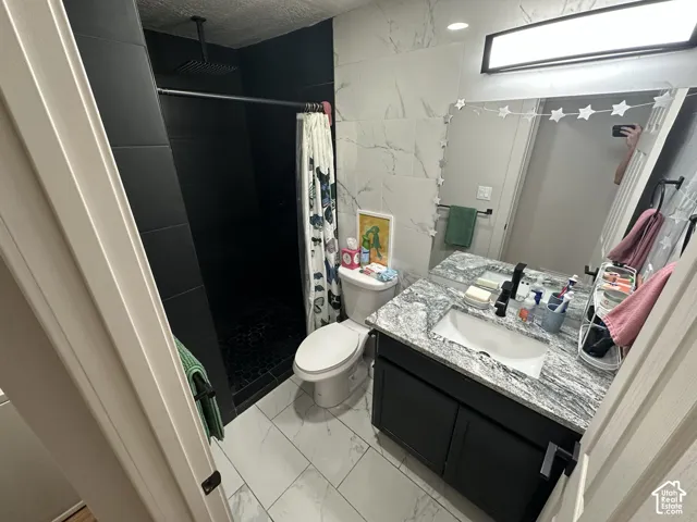 Bathroom featuring a vanity with stone countertop and integrated sink, matte black hardware, rainfall showerhead, and contrasting tile finishes