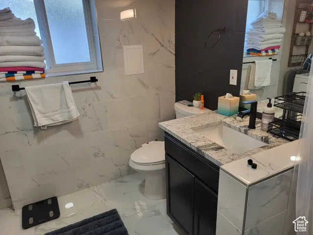 Bathroom featuring stone-finish countertop, dark cabinetry, matte black faucet, and large-format porcelain wall tiling with contrasting dark tile accent