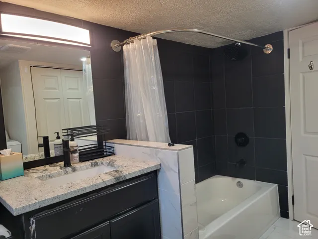 Bathroom featuring a dark wood vanity with a stone countertop, an integrated rectangular sink, matte black fixtures, and a tub-shower combination enclosed by floor-to-ceiling dark tile