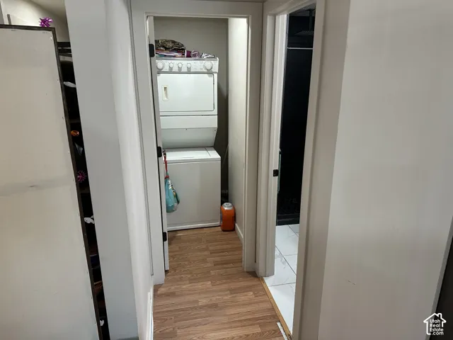 Laundry area featuring a stacked washer and dryer, wood-finish flooring, and a doorway opening to a tiled room